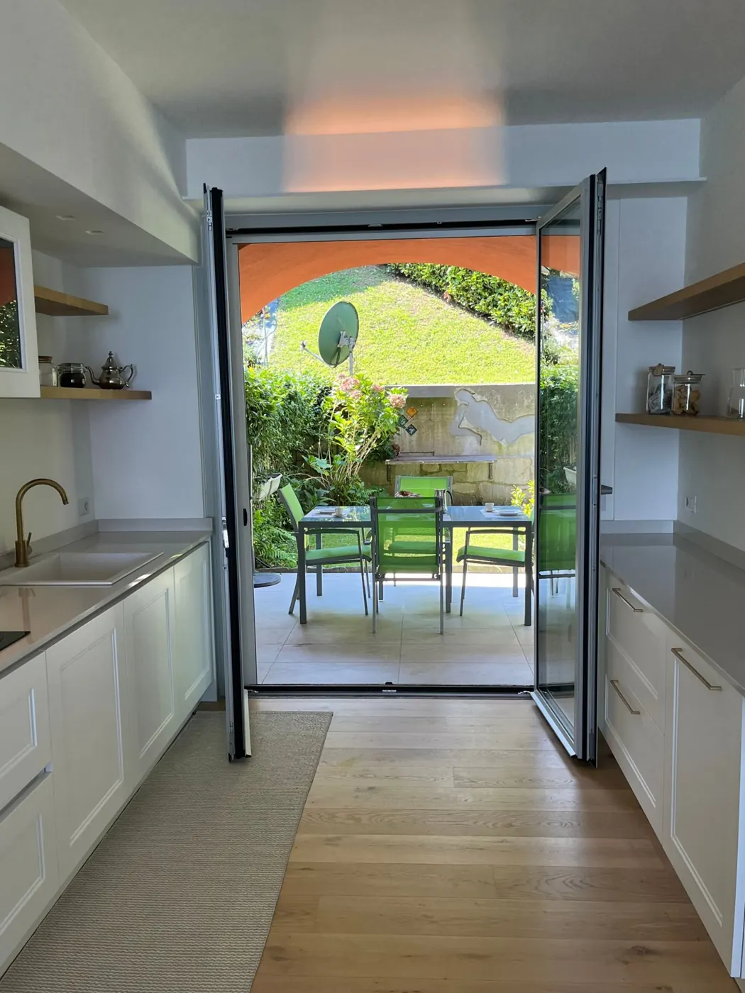 White kitchen opening onto the shaded garden patio with dining table