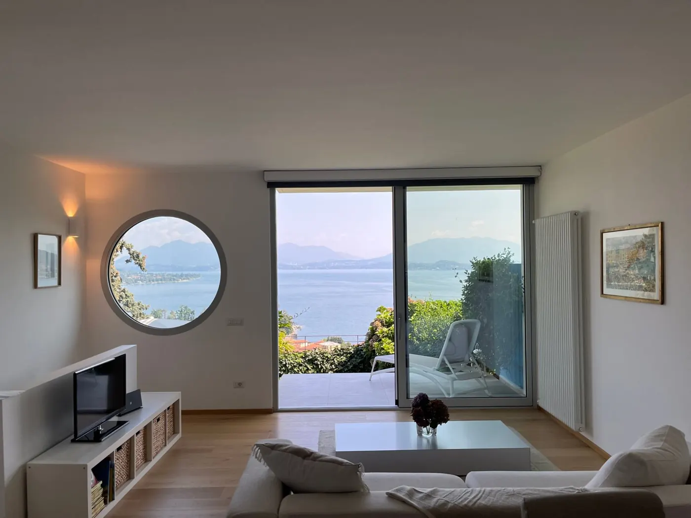 Living room with sofa, round porthole window and sliding glass doors onto the lake-view terrace